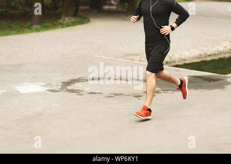 Sportlicher Mann in Ohrhörer Joggen im Park Stockfoto