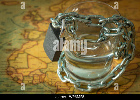 Glas Wasser in einer Kette gewickelt und mit einem Vorhängeschloss. Welt Karte als Hintergrund. Das Konzept des Problem der kleinen Trinkwasser Stockfoto