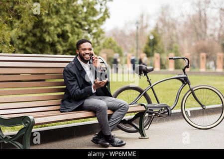 Kaffeepause. Geschäftsmann sitzt auf der Bank neben dem Fahrrad Stockfoto