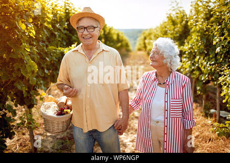 Lächelnd senior Winzer wandern in zwischen den Reihen von Reben Stockfoto
