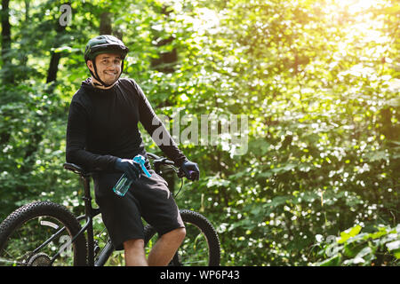 Freundliche Radfahrer holding Flasche Wasser, in die Kamera lächeln Stockfoto