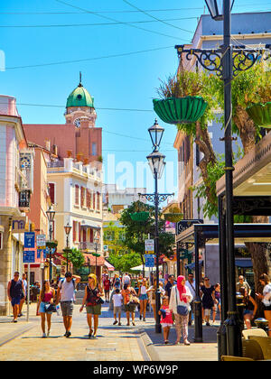 Touristen zu Fuß auf einer Hauptstraße im sonnigen Tag, mit dem Glockenturm der Heiligen Maria der gekrönte Dom im Hintergrund. Gibraltar. UK. Stockfoto