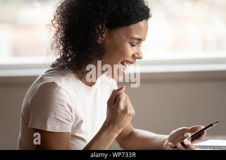 Biracial Frau Triumph empfangen Nachricht auf Handy begeistert Stockfoto