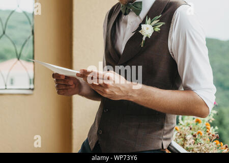 Nahaufnahme einer Bräutigam hält ein Blatt Papier in seinen Händen mit einem Eid oder eine Einladung. Vorbereitung auf die Hochzeit. Stockfoto