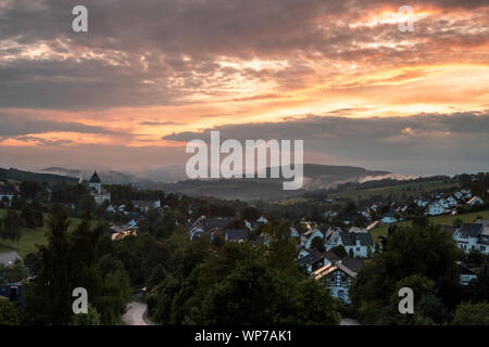 Panoramablick über die bergige Spa Village von Grafschaft im Winter Sport Region Sauerland, Deutschland, während ein farbenfroher Sonnenuntergang Stockfoto
