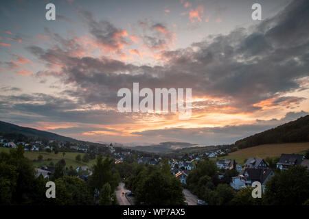 Panoramablick über die bergige Spa Village von Grafschaft im Winter Sport Region Sauerland, Deutschland, während ein farbenfroher Sonnenuntergang Stockfoto