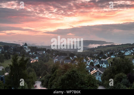 Panoramablick über die bergige Spa Village von Grafschaft im Winter Sport Region Sauerland, Deutschland, während ein farbenfroher Sonnenuntergang Stockfoto