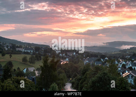 Panoramablick über die bergige Spa Village von Grafschaft im Winter Sport Region Sauerland, Deutschland, während ein farbenfroher Sonnenuntergang Stockfoto