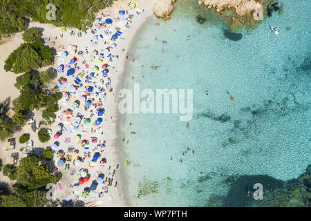 Ansicht von oben, einen atemberaubenden Blick auf einen wunderschönen Strand voll von bunten Sonnenschirmen und Menschen schwimmen im türkisblauen Wasser. Stockfoto