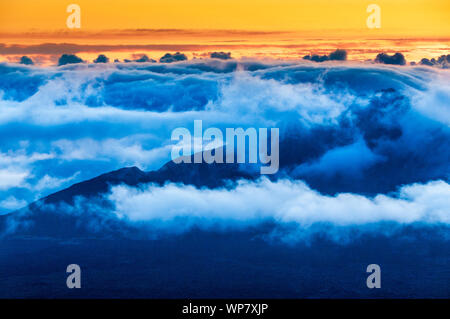 Sonnenaufgang über den Wolken und Berge in der Ferne von der Oberseite des Haleakala Kraters, Maui, Hawaii, USA Stockfoto