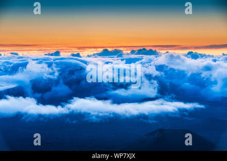 Sonnenaufgang über den Wolken und Berge in der Ferne von der Oberseite des Haleakala Kraters, Maui, Hawaii, USA Stockfoto