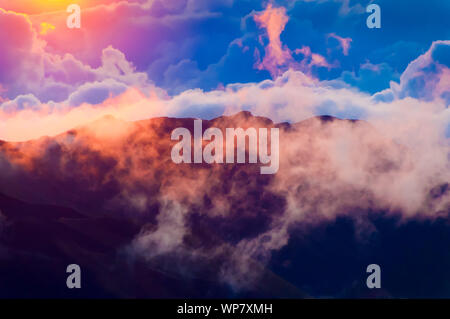 Sonnenaufgang über den Wolken und Berge in der Ferne von der Oberseite des Haleakala Kraters, Maui, Hawaii, USA Stockfoto