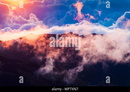 Sonnenaufgang über den Wolken und Berge in der Ferne von der Oberseite des Haleakala Kraters, Maui, Hawaii, USA Stockfoto