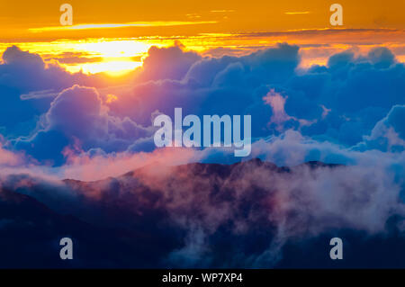 Sonnenaufgang über den Wolken und Berge in der Ferne von der Oberseite des Haleakala Kraters, Maui, Hawaii, USA Stockfoto