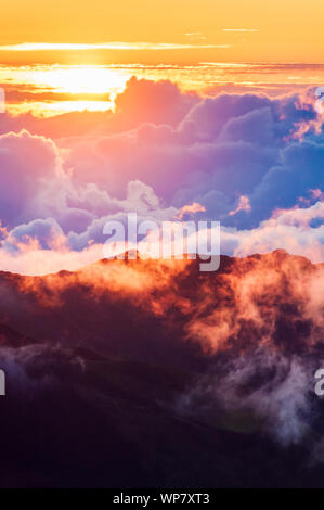 Sonnenaufgang über den Wolken und Berge in der Ferne von der Oberseite des Haleakala Kraters, Maui, Hawaii, USA Stockfoto
