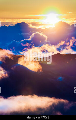 Sonnenaufgang über den Wolken und Berge in der Ferne von der Oberseite des Haleakala Kraters, Maui, Hawaii, USA Stockfoto