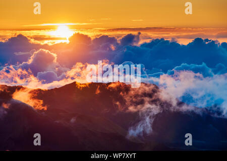 Sonnenaufgang über den Wolken und Berge in der Ferne von der Oberseite des Haleakala Kraters, Maui, Hawaii, USA Stockfoto
