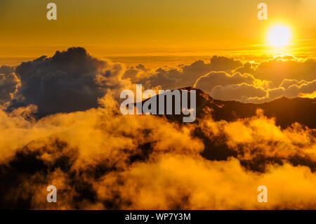 Sonnenaufgang über den Wolken und Berge in der Ferne von der Oberseite des Haleakala Kraters, Maui, Hawaii, USA Stockfoto