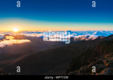 Sonnenaufgang über den Wolken und Berge in der Ferne von der Oberseite des Haleakala Kraters, Maui, Hawaii, USA Stockfoto