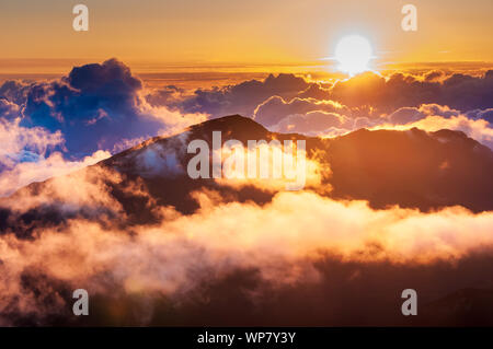Sonnenaufgang über den Wolken und Berge in der Ferne von der Oberseite des Haleakala Kraters, Maui, Hawaii, USA Stockfoto