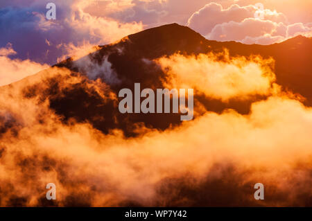 Sonnenaufgang über den Wolken und Berge in der Ferne von der Oberseite des Haleakala Kraters, Maui, Hawaii, USA Stockfoto