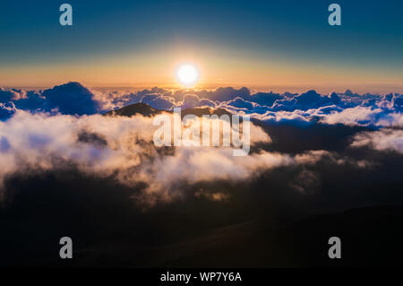 Sonnenaufgang über den Wolken und Berge in der Ferne von der Oberseite des Haleakala Kraters, Maui, Hawaii, USA Stockfoto