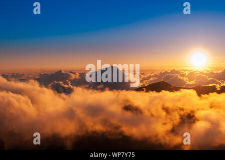 Sonnenaufgang über den Wolken und Berge in der Ferne von der Oberseite des Haleakala Kraters, Maui, Hawaii, USA Stockfoto