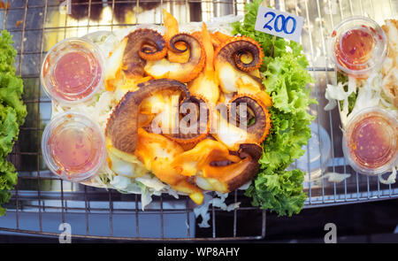 Gegrillter Tintenfisch mit Chilisauce, gehackten Kohl, und Kopfsalat. Bei einem Street Food Markt Asiatique sun der Riverfront in Bangkok, Thailand. Stockfoto