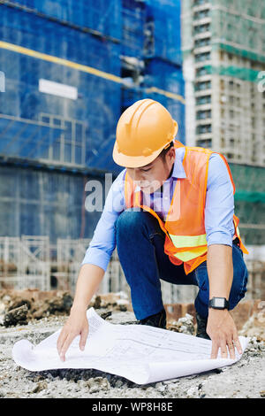 Professionelle asiatische Bauingenieur ausbreiten Gebäude Entwurf auf dem Boden und Prüfung der Grundriss Stockfoto