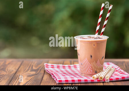 Eis Schokolade Milchshake in Einweg Plastikbecher mit waffelröllchen auf hölzernen Tisch im Freien Stockfoto