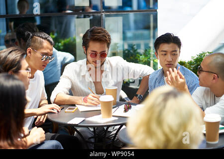 Junge asiatische Studenten in eine Diskussion in der Gruppe an einer im Coffee Shop Stockfoto