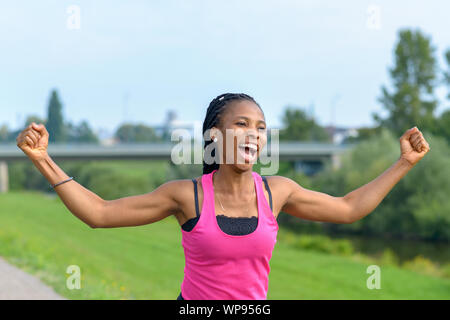 Temperamentvolle junge afrikanische Frau Jubel, wie Sie entlang einer ländlichen Pfad stanzen die Luft mit ihren Fäusten in Überschwang läuft Stockfoto