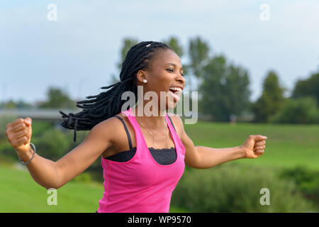 Temperamentvolle junge afrikanische Frau Jubel, wie Sie entlang einer ländlichen Pfad stanzen die Luft mit ihren Fäusten in Überschwang läuft Stockfoto