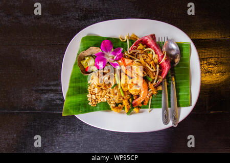 Thai gebratene Nudeln "Pad Thai" mit Garnelen und Gemüse auf die weiße Keramik Teller dekoriert mit Orchidee auf dunklen, hölzernen Tisch. Wählen Sie konzentrieren. Stockfoto