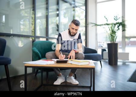 Stilvolle Geschäftsmann sitzt auf einem Sessel und Abfüllung in Dokumenten Stockfoto