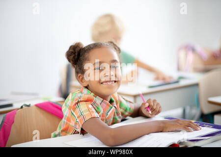 Dark-eyed girl Gefühl freudiger während am Schreibtisch sitzen und schreiben Stockfoto