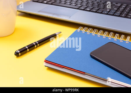 Laptop, Notebook, Smartphone und Stift auf gelben Hintergrund. Büro Schreibtisch Tisch mit modernen Accessoires Stockfoto