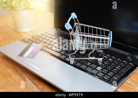 Laptop, kleinen Einkaufswagen oder Karre und Kreditkarte auf Holztisch. Internet Shopping Konzept Stockfoto