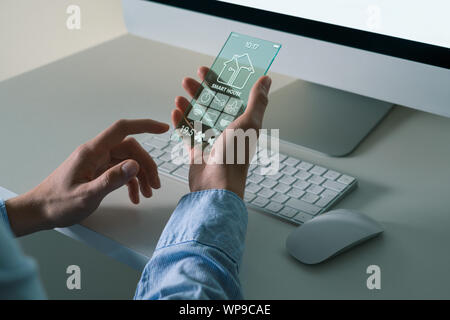 Ein Mann mit einem futuristischen transparente Telefon mit Anwendung für control Smart House. Stockfoto