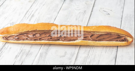 Die Hälfte der Baguette mit Schokoladencreme auf dem hölzernen Tisch Stockfoto