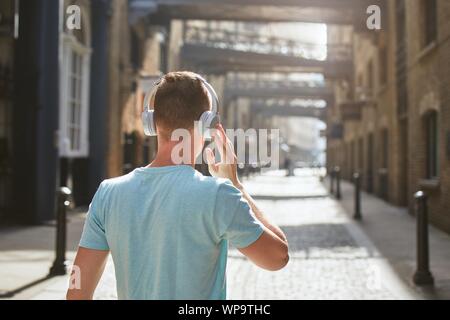 Junger Mann mit Kopfhörern Musik hören gegen alte city Street am Morgen Licht. London, Vereinigtes Königreich. Stockfoto