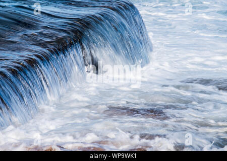 Starke Nachmittag, eingehende Flut mit Wellen, die auf eine Flutwelle pool Wand- und die Schaffung eines leistungsfähigen Überlauf schäumenden Brandung als Nachwirkung Absturz Stockfoto