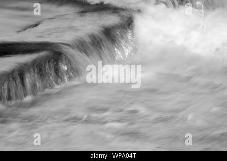 Schwarze und Weiße abstrakte Fotografien einer Meereslandschaft mit starken Rückspülen mit Wasser über eine Flutwelle pool Wand auf einem niedrigen Verschlusszeit fließende Stockfoto