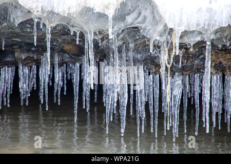 Eiszapfen hängen von snowy Steine über Flusswasser. Kirgisistan Stockfoto