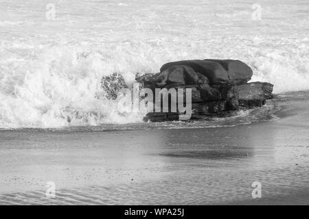 Eine schöne Schwarze und Weiße Meereslandschaft mit heiteren und schäumenden Wasser. Die Wellen sind krachend gegen einen Felsen am späten Nachmittag. Stockfoto