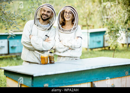 Porträt eines Mannes und einer Frau die Imker in Schützende Uniform stehen zusammen auf dem kleinen traditionellen Bienenhaus mit hölzernen Bienenstöcke Stockfoto