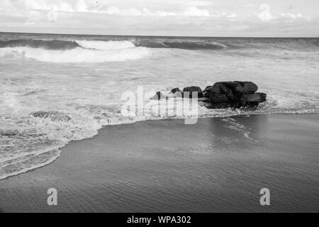 Eine schöne Schwarze und Weiße Meereslandschaft mit heiteren und schäumenden Wasser. Die Wellen sind krachend gegen einen Felsen am späten Nachmittag. Stockfoto