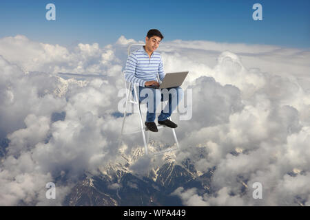 Junger Mann, der mit einem Laptop auf einer Leiter sitzt Stockfoto