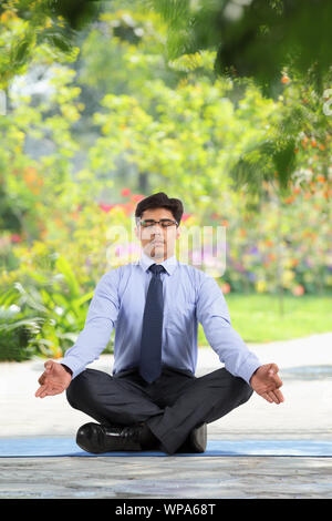 Geschäftsmann sitzt in Yoga-Pose auf einem Rasen Stockfoto
