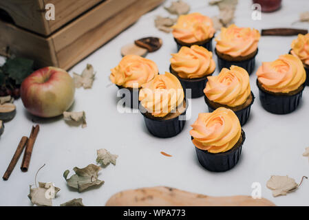 Herbst gelb und orange Cupcakes auf hellem Hintergrund mit Herbst Laub, Kürbisse und Äpfel. Herbst Süßigkeiten mit Sahne für Kinder. Karotte Cupcakes auf Herbst Hintergrund Stockfoto